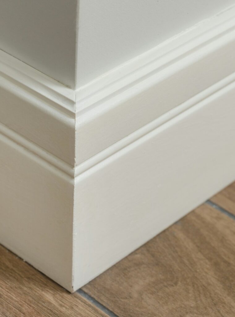 Molding in the interior, baseboard corner. Light matte wall with tiles immitating hardwood flooring